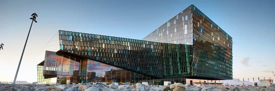 Opern- und Konzerthaus Harpa in Reykjavik mit gläserner Fassade und Fensterflächen vor einem steinigen Boden.