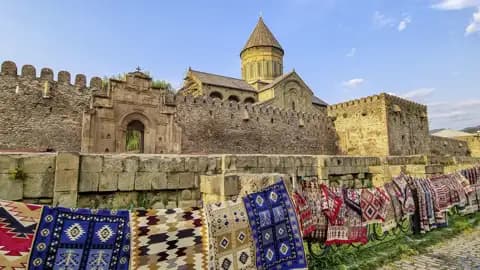 Bunte, traditionelle Teppiche hängen an einem Geländer vor der historischen Swetizchoweli-Kathedrale in Mzcheta, Georgien.